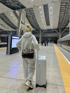 a woman is walking with her luggage at the train station while waiting for someone to board