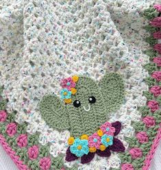 a crocheted blanket with a green teddy bear on it's side and flowers around the edges