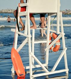 two people standing on a lifeguard chair in the water at the beach with an orange life preserver attached to it