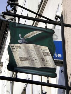 a sign hanging from the side of a building with an open book on it's back