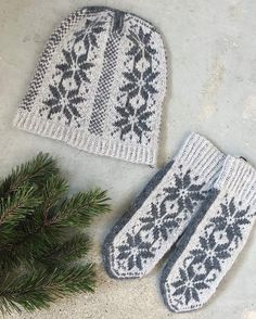 two knitted mittens sitting next to a pine branch on top of a cement floor