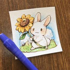 a drawing of a bunny holding a sunflower on top of a wooden table next to a blue marker