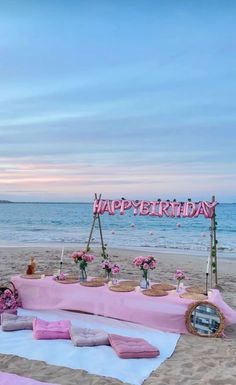 an outdoor birthday party setup on the beach with pink and white decorations, flowers and candles