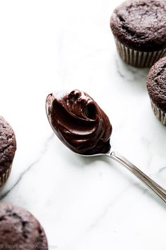 chocolate cupcakes with frosting on a marble counter top and one being held by a spoon