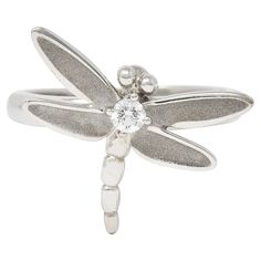 Designed as a stylized dragonfly with brushed matte wings, Centering a prong set round brilliant cut diamond. Weighing approximately 0.10 carat total. Eye clean and bright. With high polish finish. Stamped 750 for 18 karat gold. Fully signed for Tiffany & Co.. Circa: 2000's. Ring size: 5 3/4 and sizable. Measures North to South 18.0 mm and sits 3.5 mm high. Total weight: 4.5 grams. Stock Number: We-11179 Dragonfly Ring, Contemporary Ring, Tiffany And Co, Round Brilliant Cut Diamond, Brilliant Cut Diamond, Estate Jewelry, Tiffany & Co., Round Brilliant, Diamond White