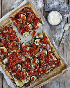 a pizza with tomatoes, zucchini and other toppings sitting on top of a wooden table