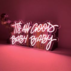 a neon sign that says it's all good baby, in front of some books