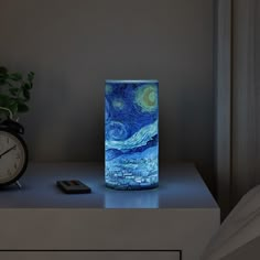 an alarm clock sitting on top of a table next to a vase with a painting