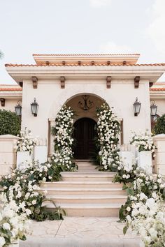 an entrance to a house with white flowers and greenery on the steps leading up to it