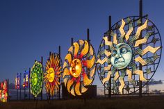 a row of colorful lights on poles in front of a sky filled with clouds and sun