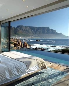 a large bed sitting next to a window overlooking the ocean and mountains in front of it