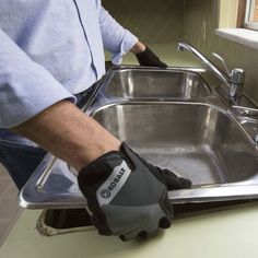 a man in black gloves is washing a silver sink