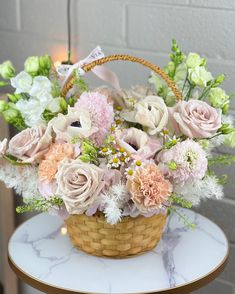 a basket filled with lots of flowers on top of a white marble topped table in front of a brick wall