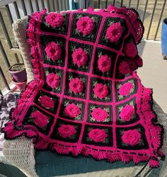 a crocheted blanket with pink flowers on it sitting on a wicker chair