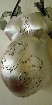 a silver mask hanging on the wall next to a vase with flowers and leaves in it