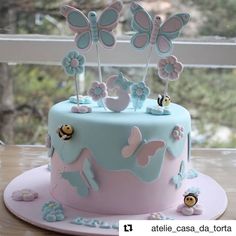 a blue and pink cake with butterflies on top is sitting on a table next to a window