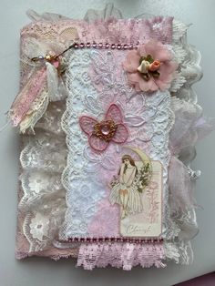 a pink and white altered art piece with laces, flowers, and angel wings