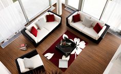 a living room filled with white and red couches next to large glass windows on top of a hard wood floor