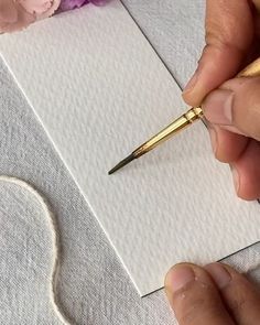 a person holding a pen and writing on a piece of paper with flowers in the background