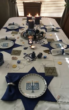 the table is set for hanukkah with candles on it and plates in front of them