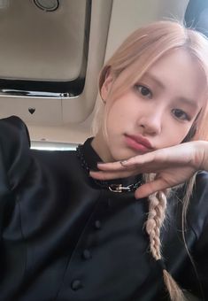 a young woman with blonde hair wearing a black shirt and chain necklace, sitting in a car