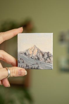 a person holding up a small card with a mountain scene in the backgroun