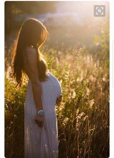 a pregnant woman standing in tall grass at sunset