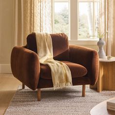 a brown chair with a blanket on it in front of a window and a table