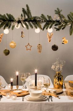 a dining room table set for christmas with candles and ornaments hanging from the ceiling over it