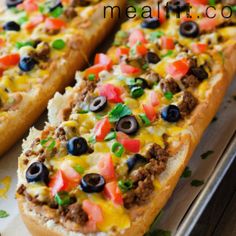 two long breads with cheese, black olives and tomatoes on them sitting on a tray