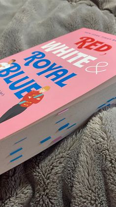 a pink book sitting on top of a bed next to a gray and white blanket