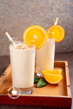 two glasses filled with orange juice on top of a wooden tray