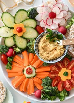 a white plate topped with lots of veggies and hummus next to crackers