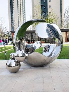 a large metal sculpture sitting on top of a cement floor next to a park filled with green grass