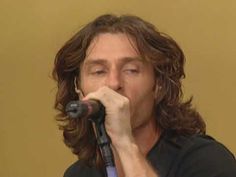 a man with long hair holding a microphone to his mouth and singing into the mic