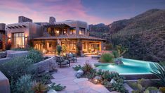 a large house with a pool in front of it at sunset or dawn, surrounded by greenery and rocks