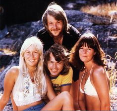 three women and one man are sitting on the ground in front of some rocks, smiling at the camera