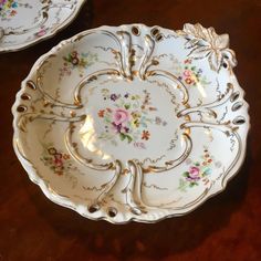 two white plates with floral designs on them sitting on a wooden table next to each other