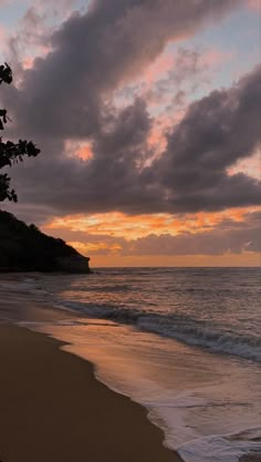 the sun is setting over the ocean with clouds in the sky and trees on the beach