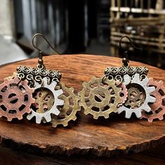 two pairs of earrings with gears on them sitting on top of a piece of wood