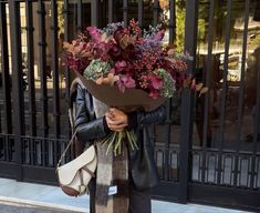 a woman is walking down the street with flowers on her head and holding a purse