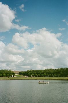 a boat floating on top of a lake next to a lush green park under a cloudy blue sky