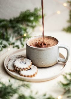 a cup of hot chocolate being poured into a mug with two cookies on the side