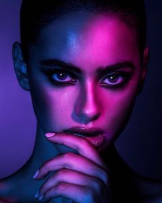 a woman with dark makeup and purple light on her face, posing for the camera