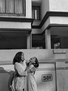 two women standing next to each other in front of a building