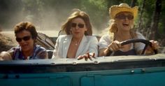 three women are riding in the back of a blue truck and one woman is wearing sunglasses