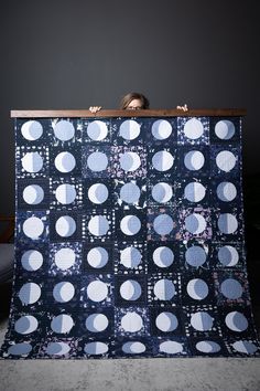 a woman is hiding behind a quilt with white circles on blue fabric and she has her head over the edge