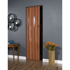 a tall wooden door stands in front of a gray wall and wood floored area