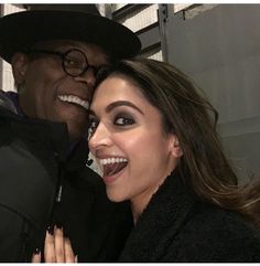 a man standing next to a woman in a black coat and hat smiling at the camera