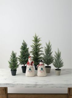 three potted christmas trees sitting next to each other on a white table with santa